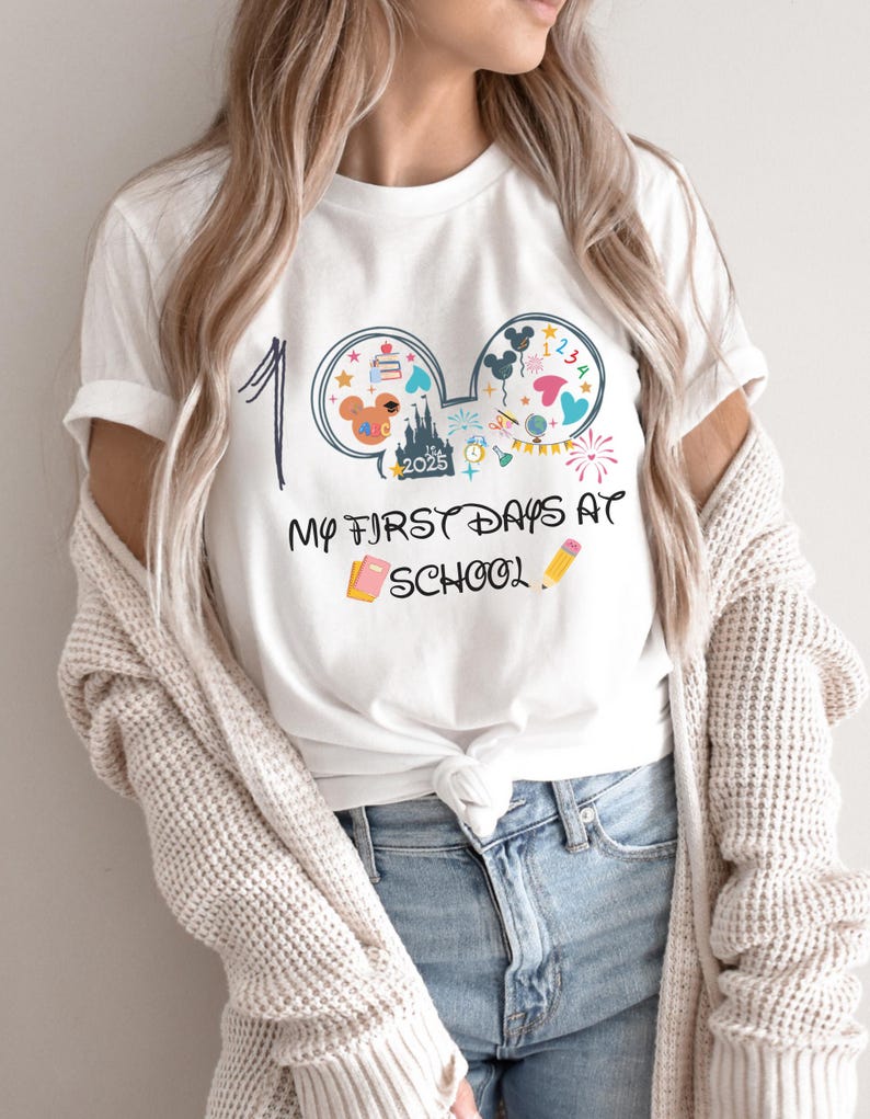 May include: White t-shirt with a colorful graphic design featuring Mickey Mouse ears, a castle, and the text "My First Days at School 2025." The design includes a number 1, a book, and a pencil.
