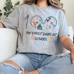 May include: A gray t-shirt with a colorful graphic design featuring Mickey Mouse ears, a castle, and the text "My First Days at School." The shirt also includes the number "1" and the year "2025."
