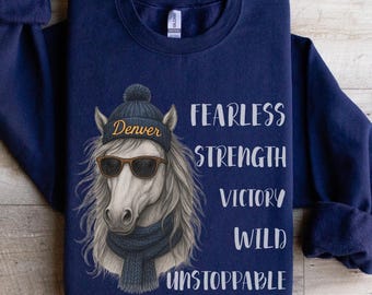Puede incluir: Sudadera azul marino con un gráfico de un caballo con gorro, gafas de sol y bufanda. La palabra "Denver" está en el sombrero. El texto a la derecha dice "FEARLESS, STRENGTH, VICTORY, WILD, UNSTOPPABLE."