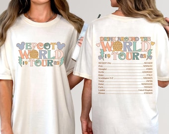 May include: Cream-colored t-shirt with a colorful retro design. The front features the text "EPCOT WORLD TOUR 1982" with a globe graphic. The back says "DRINK AROUND THE WORLD TOUR 1982" with a list of cities. A fun, vintage-inspired tee.