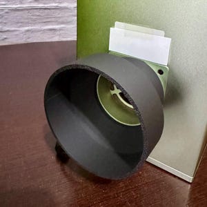 Può includere: Un filtro dell'aria in schiuma nera per un motore di auto. Il filtro è attaccato a un alloggiamento in metallo argentato con una superficie verniciata di verde.