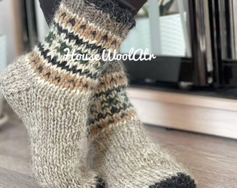 Puede incluir: Un par de calcetines cálidos y peludos hechos de lana. Los calcetines tienen un patrón geométrico negro, marrón y verde. Los calcetines se muestran sobre un suelo de madera.
