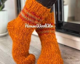 May include: A pair of orange wool socks with red and gray stripes. The socks are knitted and have a fuzzy texture. The text "House Wool Attr" is visible on the socks.