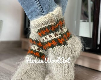 Puede incluir: Un par de calcetines de lana grises con un colorido patrón de rayas naranjas, verdes y blancas. Los calcetines son gruesos y parecen hechos a mano, con el texto "HouseWoolArt" visible.
