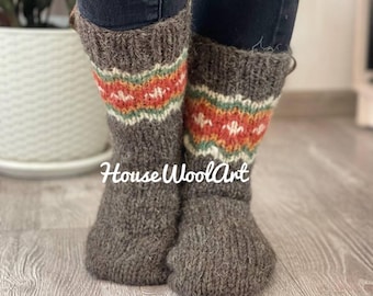 May include: A pair of gray wool socks with a colorful patterned band featuring orange, white, and green designs. The socks are knee-high and appear to be handmade. The text "House WoolArt" is visible on the socks.