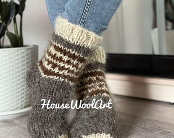 May include: Cozy, hand-knitted wool socks in shades of gray, brown, and cream. The socks feature a textured design with a ribbed cuff and a patterned section. The text "House WoolArt" is visible on the socks.