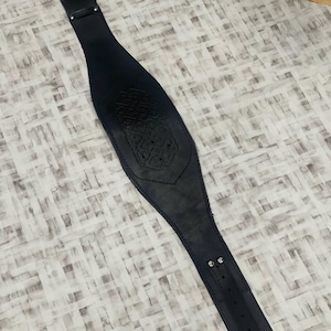 May include: A black leather belt with an embossed design. The belt features a buckle and adjustment holes. The belt is approximately 76 cm long. The design is in the center.