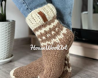 May include: Hand-knitted wool socks in shades of brown and cream, with a geometric pattern and a leather tag. The socks have a thick, textured appearance and are designed to keep feet warm. The text "House WoolArt" is visible on the socks.