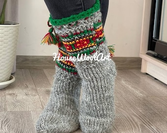 May include: Gray knitted socks with a green, red, and yellow patterned cuff. The socks have a decorative tassel and the text "House WoolArt" is visible. These cozy socks are perfect for cold weather.
