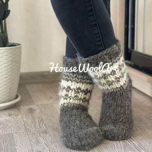 May include: Gray and white knit wool boot socks. The socks have a striped pattern in the middle and are labeled "HouseWoolArt". The socks are thick and appear warm.