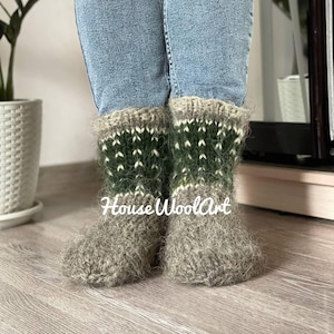 May include: Cozy, handmade wool socks in shades of gray, green, and white. The socks feature a patterned design around the ankle and are worn with blue jeans. The text "House WoolArt" is visible on the socks.