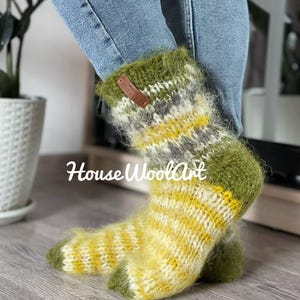 May include: Cozy, hand-knitted socks in shades of yellow, green, and gray. The socks feature a striped pattern and a fluffy texture. The text "House WoolArt" is visible on the image. These warm socks are perfect for cold weather.