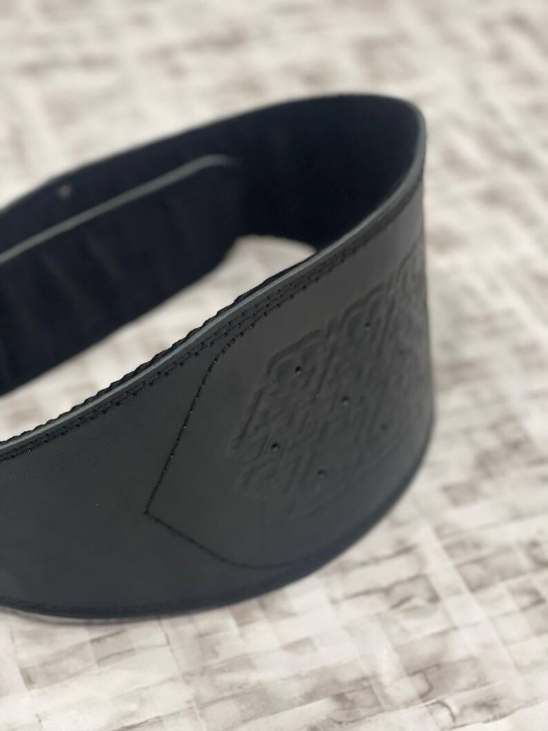 May include: A black weightlifting belt with an embossed pattern. The belt is made of a thick, durable material and has detailed stitching. It is designed to provide support during heavy lifting exercises. The belt's width is approximately 10 cm.