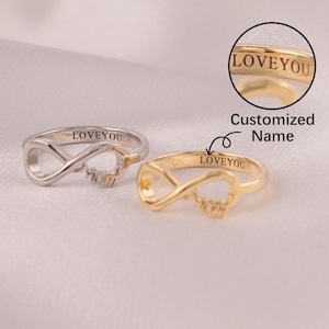 May include: Two rings, one silver and one gold, each featuring an infinity symbol design. The rings have the word "LOVEYOU" engraved on them. The image also includes the text "Customized Name".