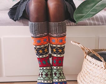 May include: A pair of colorful, patterned knee-high socks with a pink toe and heel. The socks are made of a soft, knitted fabric and feature a geometric design in shades of red, orange, yellow, green, blue, and black.
