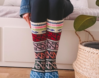 May include: A pair of colorful knitted socks with geometric patterns in shades of blue, pink, red, green, and white. The socks are knee-high and have a white cuff.