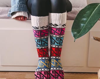May include: Knee-high socks with a colorful geometric pattern. The socks feature a white cuff, followed by bands of pink, red, blue, and yellow designs. The toes are light blue. These cozy socks are perfect for cold weather.
