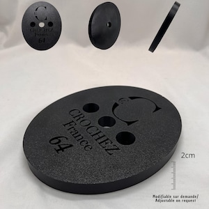 Op de afbeelding: Zwart ovaalvormig product met de tekst "CROCHEZ France 64" en een cirkelvormig logo. Het product heeft drie gaten en een liniaal van 2 cm is afgebeeld. Extra stukken zijn te zien in de afbeelding. De tekst "Modifiable sur demande/ Adjustable on request" is ook zichtbaar.
