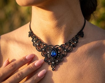 May include: A black macrame necklace featuring an intricate woven cord design with a central teardrop-shaped blue gemstone and small white beads integrated throughout the pattern, secured with a thin black cord around the neck.