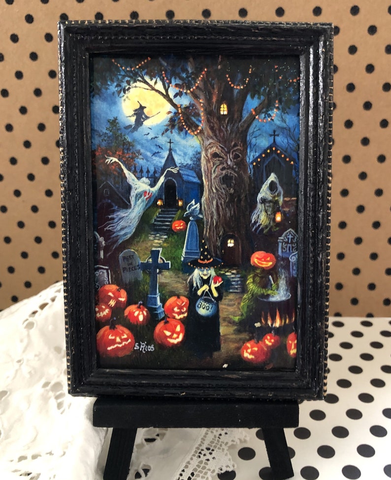 May include: A framed Halloween-themed painting depicting a witch with a cauldron, a ghost, and a spooky tree with jack-o'-lanterns. The painting is set against a dark blue background with a full moon and stars. The text "Rest in Pieces" and "Boo!" are visible on the painting.