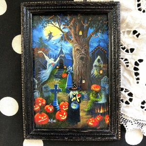 May include: A framed painting of a Halloween scene with a witch, a graveyard, and a spooky tree. The witch is holding a bucket of candy and a red apple. The graveyard has a tombstone that reads "Rest in Pieces". The tree has a face carved into it and is decorated with lights. The painting is set against a dark blue background with a full moon.