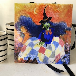 May include: A watercolor painting of a witch with a black cat sitting on her lap. She is wearing a blue dress and a black hat. The background is a colorful sunset with a crescent moon.