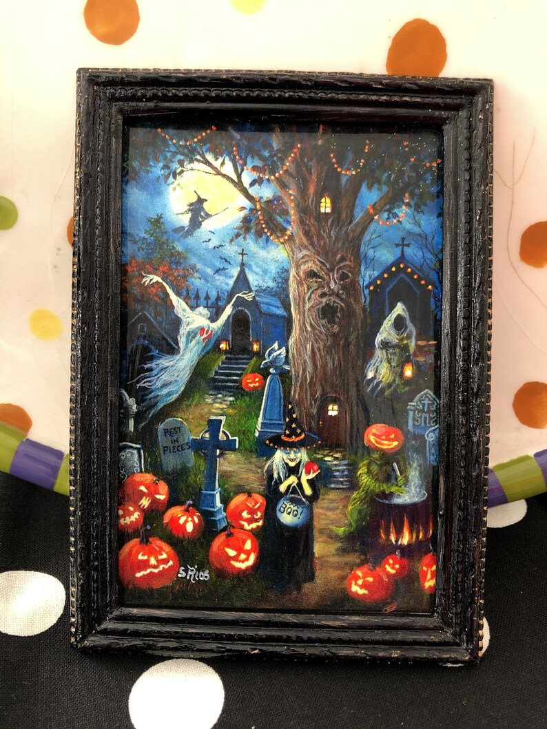 May include: A framed painting of a spooky Halloween scene with a witch, a graveyard, and jack-o'-lanterns. The painting is set against a dark blue background with a full moon in the sky. The witch is wearing a black dress and a pointed hat, and she is holding a cauldron. The graveyard is filled with tombstones and crosses, and there are jack-o'-lanterns scattered throughout the scene. The painting is signed "S. Rios".