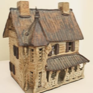 May include: A ceramic house model with a brown roof, white walls, and a porch. The house has a detailed design with windows and a chimney.