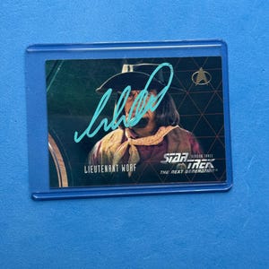 May include: A Star Trek: The Next Generation trading card featuring Lieutenant Worf. The card has a green and gold background with the Star Trek logo and "Season Three" text. The card is encased in a protective plastic sleeve, and has a signature in blue ink.