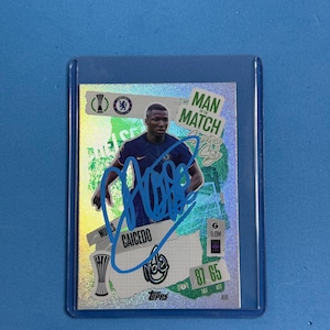 May include: A collectible trading card featuring a soccer player in a blue jersey. The card has a holographic background with the text "Man of the Match" and the player's name, CAICEDO, and signature. The card is in a protective sleeve.