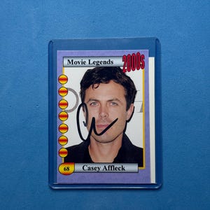 May include: A Casey Affleck trading card from the Movie Legends 2000s series. The card features a headshot of the actor, his signature, and the number 68. The card is encased in a protective plastic sleeve.