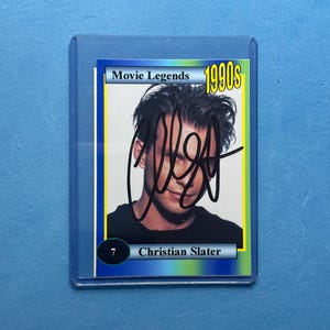 May include: A trading card featuring actor Christian Slater from the 1990s. The card is labeled "Movie Legends" and has a yellow and blue border. The card is encased in a clear plastic sleeve.
