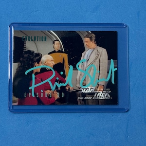 May include: A Star Trek: The Next Generation trading card in a protective sleeve. The card features a scene from the episode "Evolution" with the text "Riker's Autograph" in teal script. The card is set against a blue background.