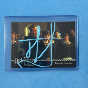 Puede incluir: Una tarjeta coleccionable de Harry Potter de "Prisonero de Azkaban" con el texto "Teaching Riddikulus". La tarjeta está en una funda protectora. La imagen muestra al profesor Lupin y a Harry Potter.