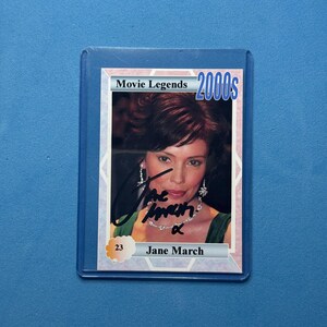 Op de afbeelding: Een verzamelkaart uit de serie "Movie Legends 2000s", met een portret van Jane March. De kaart zit in een beschermhoes en bevat een handtekening. Het nummer "23" is zichtbaar.