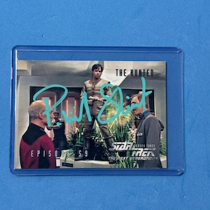 May include: A Star Trek: The Next Generation trading card in a protective sleeve. The card features a scene from the episode "The Hunted" with actors and the episode title. The card is signed by an actor.