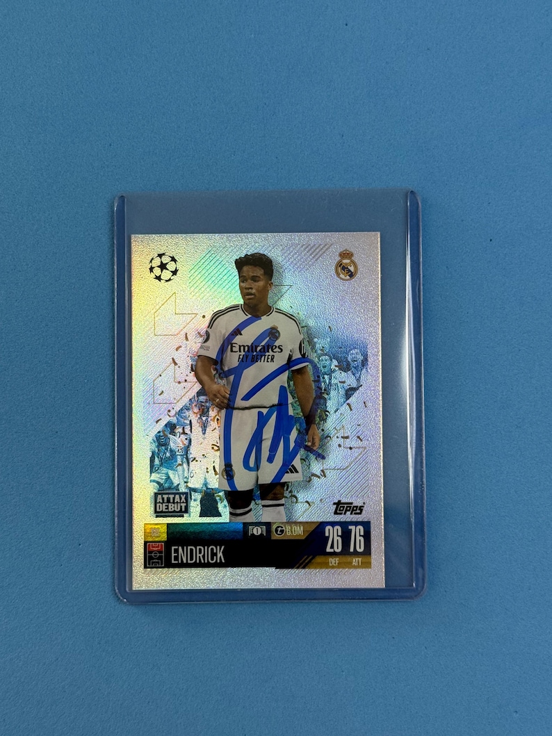 Peut inclure: Carte de collection repr&eacute;sentant un joueur de football en uniforme blanc et bleu marine, avec le logo Emirates Fly Better. La carte a un fond holographique argent&eacute; et un autographe bleu. La carte est dans une pochette de protection.