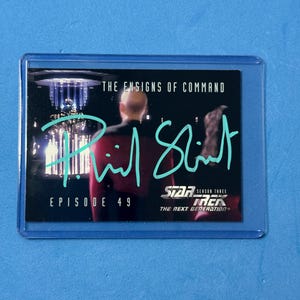 May include: A Star Trek: The Next Generation trading card in a protective sleeve. The card features the text "THE ENSIGNS OF COMMAND" and "EPISODE 49". It also includes a signature and the Star Trek logo.