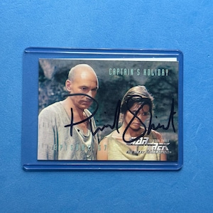 May include: A Star Trek: The Next Generation trading card featuring a photo of two actors. The card is encased in a protective sleeve. The card has the text "CAPTAIN'S HOLIDAY" and "EPISODE 67". The card is signed.