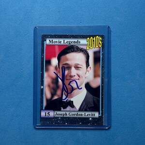 May include: A trading card featuring Joseph Gordon-Levitt from the 2010s Movie Legends series. The card has a blue signature and the text "Movie Legends 2010s" at the top. The card is encased in a protective sleeve.