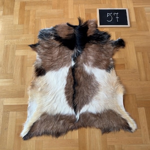 Op de afbeelding: Een bruin, wit en zwart geitenvachtenkleed met een natuurlijke, zachte textuur. Het kleed is ongeveer 145 cm lang.