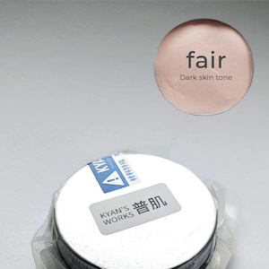 May include: A small, round container of fair skin tone makeup, with the text "KYAN'S WORKS" and Chinese characters on the label. A separate swatch displays the words "fair" and "Dark skin tone". The product is packaged in clear plastic.