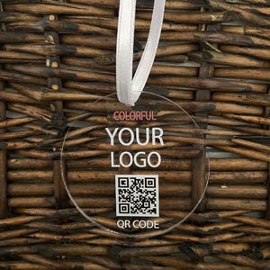 May include: A clear round acrylic bauble with a white ribbon. The bauble has the text "COLORFUL YOUR LOGO QR CODE" and a black and white QR code.