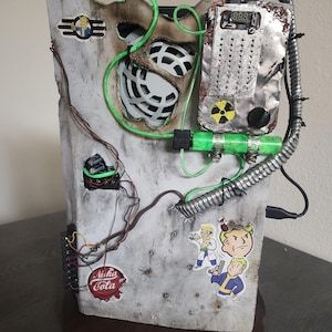 May include: A white, gray, and black computer case with a green glow, wires, and a Nuka Cola logo. The case is decorated with Fallout characters and a digital display.