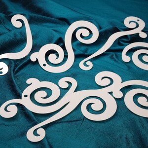 May include: White decorative swirls cut from a sheet of material, arranged in a pattern on a teal blue fabric background.
