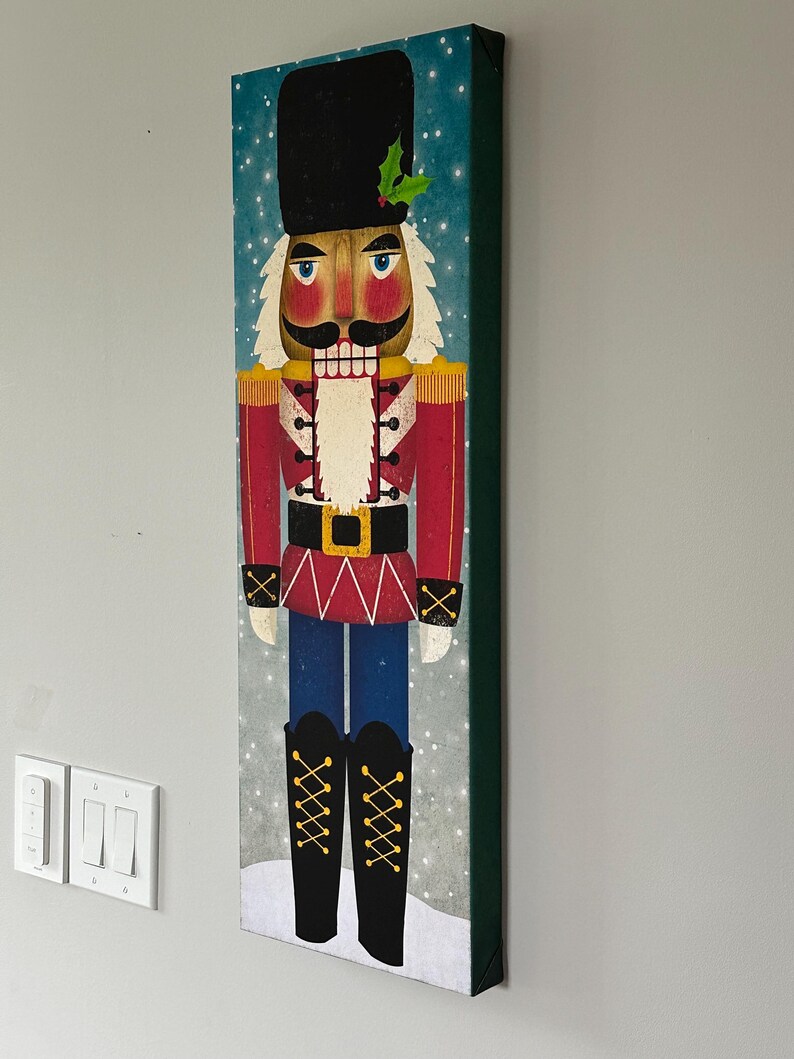 May include: A colorful illustration of a traditional nutcracker soldier with a red and white uniform, black hat, and a gold belt. The background is a blue and white snowy scene.