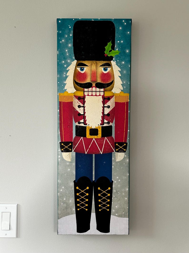 May include: A red and blue nutcracker with a black hat and a white beard. The nutcracker is standing on a snowy background with a blue sky.