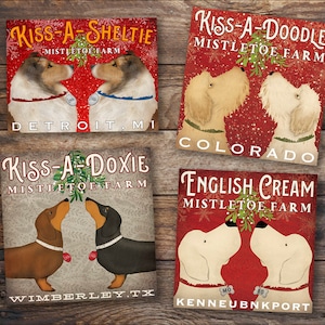 Puede incluir: Cuatro letreros navideños con perros de diferentes razas bajo el muérdago. Cada letrero tiene el nombre de la raza de perro, "Kiss-A-", y la ubicación de la granja. Los letreros están sobre un fondo de madera.