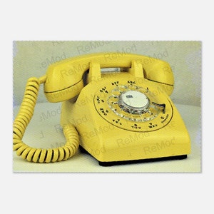 Puede incluir: Un teléfono de disco amarillo con un disco negro y un cable en espiral. El teléfono tiene un fondo blanco con un patrón de pequeños puntos.