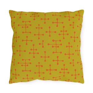 May include: Square throw pillow with a retro atomic pattern. The pillow features a mustard yellow background with a repeating pattern of orange cross and line designs. The pillow is square and appears to be made of a soft fabric.